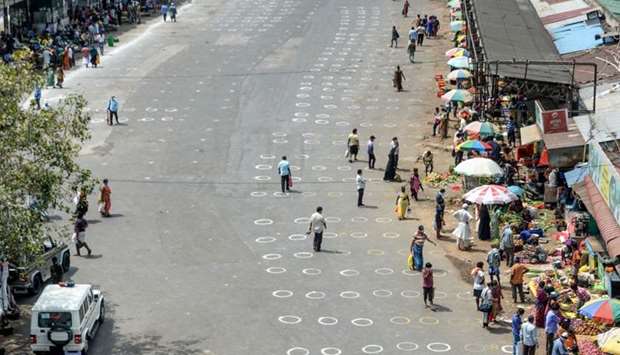 People walk in an area with circles marked on the floor for social distancing as they buy groceries at a temporary market set up at a bus stand in Chennai, India.