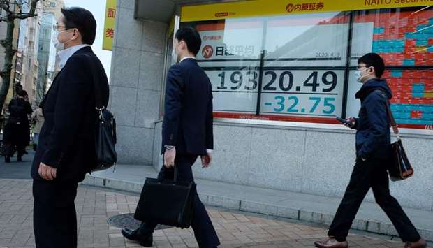 Pedestrians walk past a quotation board displaying share prices of the Tokyo Stock Exchange. The index ended flat at 19,345.77 points yesterday.