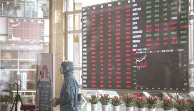 A worker wearing a protective suit stands at a temperature screening point in front of an electronic stock board at the Shanghai Stock Exchange. The Composite index closed up 1.5% to 3,477.62 points yesterday.
