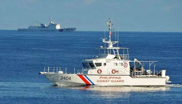 (File photo) A Philippine coast guard ship sails past a Chinese coast guard ship near Scarborough shoal in the South China Sea in May 2019. (AFP)