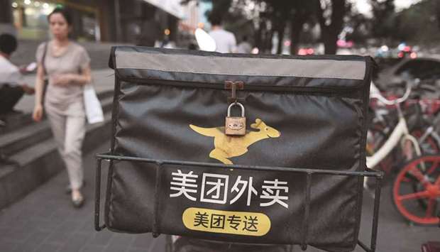 A woman walks past a Meituan delivery scooter on a sidewalk in Beijing. The probe was prompted by reports that Meituan allegedly engaged in forced exclusivity agreements with vendors, the State Administration for Market Regulation said in a statement.