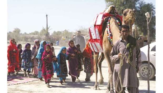 Children follow Roshan the camel, which is carrying  books to them in Mand, Pakistan.