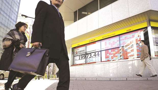 Pedestrians walk past an electronic stock board displaying the Nikkei 225 Stock Average figure outside a securities firm in Tokyo (file). The Nikkei 225 closed 0.8% down at 29,696.63 points yesterday.