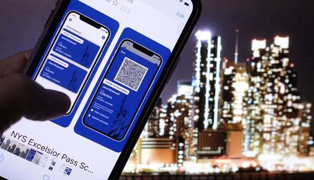 A person looking at the app for the New York State Excelsior Pass, which provides secure, digital proof of a Covid-19 vaccination, in front of a screen showing the New York skyline.