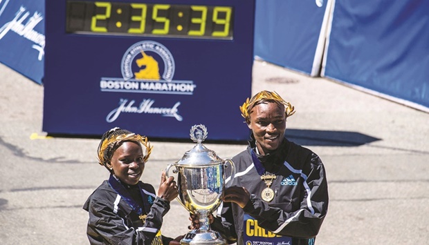 Peres Jepchirchir (left) and Evans Chebet hold the victory trophy over the finish line after both took first place in their divisions in the 126th Boston Marathon yesterday. The 26.2 mile course (42.2K) is celebrating 50 years of having an official womenu2019s division and being back to itu2019s normal April race date after cancellations and date changes due to the pandemic. (AFP)