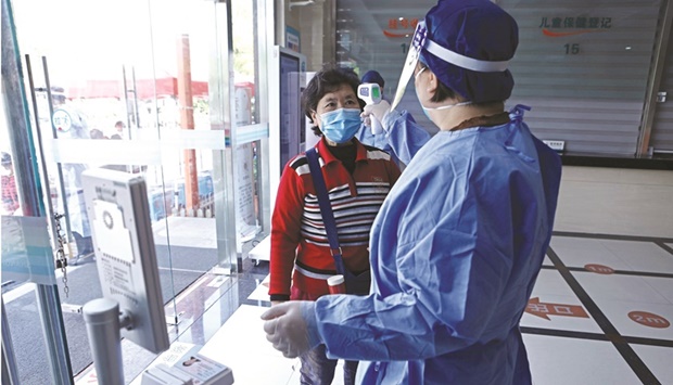 A worker in a protective suit measures the body temperature of a woman during a vaccination session against Covid-19 for elderly people, at a community health service centre in Fengxian district of Shanghai.