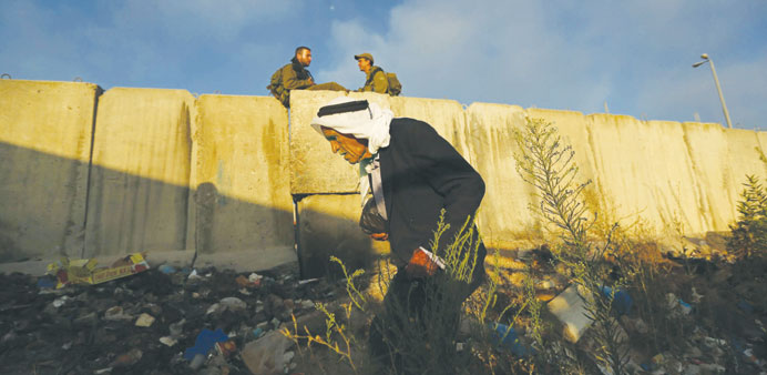    Israeli soldiers sit near a part of Israelu2019s controversial barrier as a Palestinian walks towards Qalandiya checkpoint near the West Bank city of R