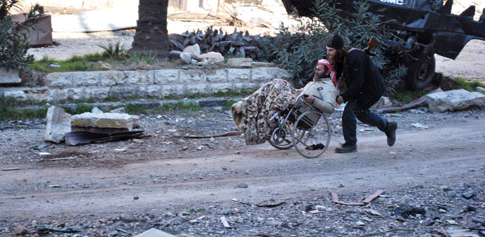 A civilian in a wheelchair is aided by an armed man ahead of being evacuated by UN staff from the besieged district of Homs yesterday.