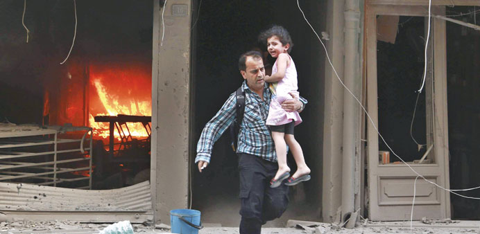 A man carrying a child runs out of a burning building at the site of a reported barrel bomb attack by regime forces in Aleppou2019s Al Shaar district yest