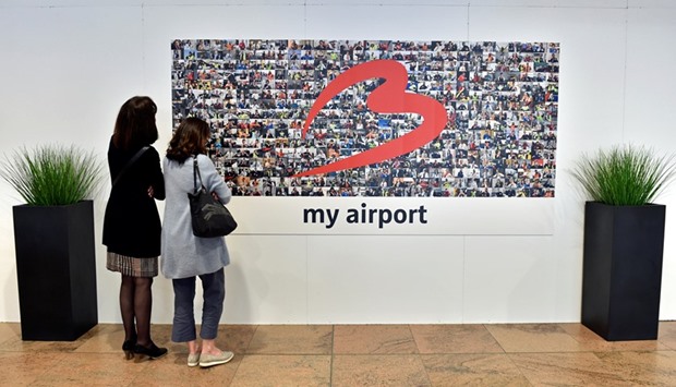 Two women view an artwork showing the faces of airport staff members in the departure hall of Brussels Airport in Zaventem.