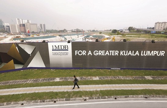 A man walks past a 1MDB billboard at the fundu2019s flagship Tun Razak Exchange development in Kuala Lumpur. Singapore authorities are conducting a wide-ranging money laundering probe into bank accounts linked to 1MDB, whose activities have triggered investigations across three continents.