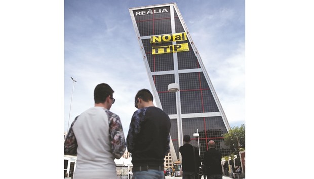 People look at Greenpeace activists displaying a banner against the TTIP free trade agreement while suspended on one of the Kio towers in Madrid.