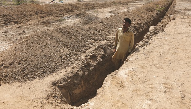 Shahid Balouch posing for a photograph in a mass grave in the cemetery, as preparations are made in case of another heatwave in Karachi.