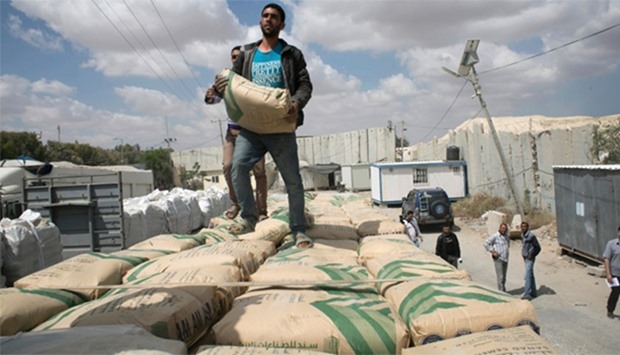 Palestinian workers stand on a truck loaded with bags of cement