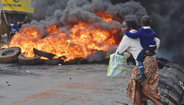 A woman carries a school pupil past a burning barricade in the Kibera slum during a demonstration of opposition supporters in Nairobi yesterday.