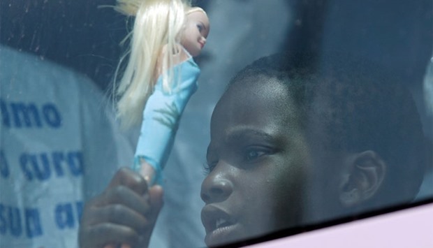 A child holds a doll as he sits in a coach after disembarking from the Italian Navy vessel Vega at the Reggio Calabria harbour, southern Italy
