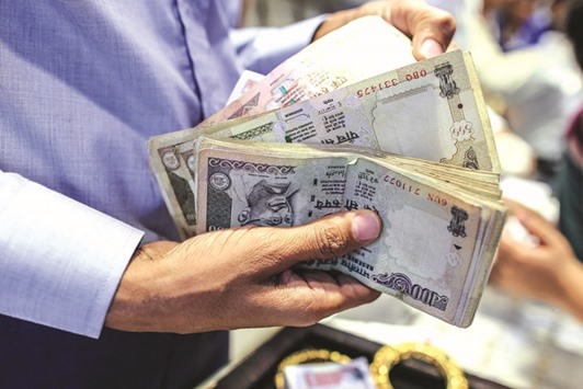 A salesperson holds Indian rupee banknotes of various denominations at a jewellery store in Mumbai. The rupee trimmed its initial gains against the American currency and closed marginally up by 2 paise to 66.42 yesterday.