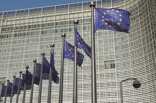 EU flags fly outside the European Commission headquarters building in Brussels. The EU told the euro areau2019s largest economies to reduce debt and modernise labour markets as it again slashed its inflation forecast and warned of slower- than-predicted growth across the 19-nation bloc.