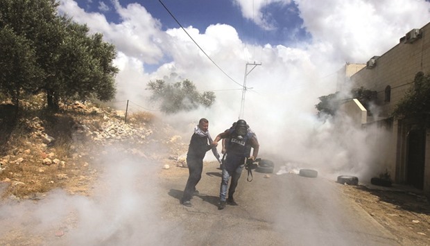 A journalist is helped by Palestinian man as he runs for cover from tear gas fired by Israeli security forces during clashes with protesters following a weekly demonstration against the expropriation of Palestinian land by Israel in the village of Kfar Qaddum, near Nablus, in the occupied West Bank yesterday.