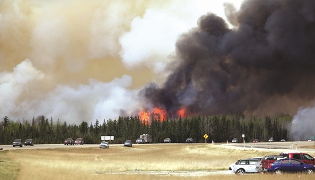 A convoy of evacuees travels south as flames rise along the highway near Fort McMurray, Alberta.