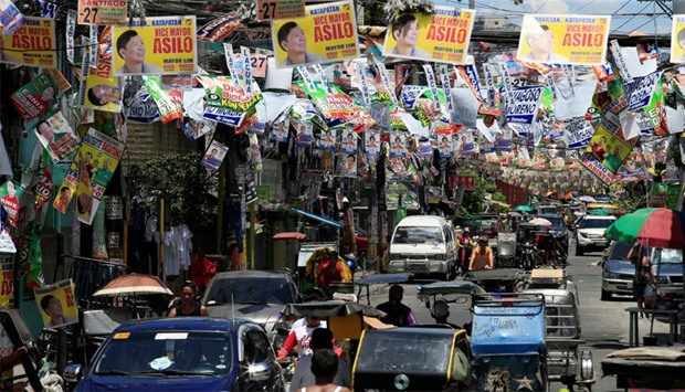 Election posters of Philippine candidates are seen hanging above vehicles driving along a main stree