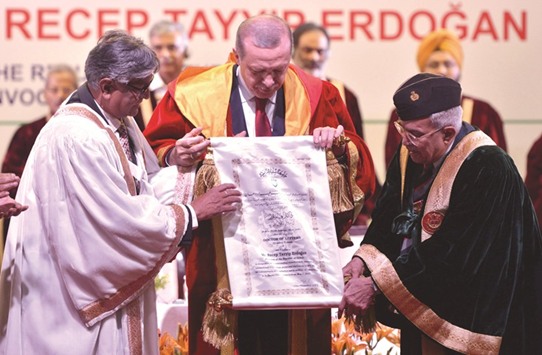 Turkish President Recep Tayyip Erdogan is assisted by officials as he displays the honorary degree he received from Jamia Millia Islamia University in New Delhi yesterday.