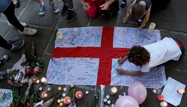 People write messages on an English national flag during a vigil for the victims of an attack on concert goers at Manchester Arena