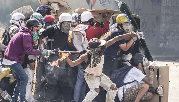 Protesters using hardhats, gloves, and gas masks take cover behind homemade shields during clashes with riot police in Caracas.