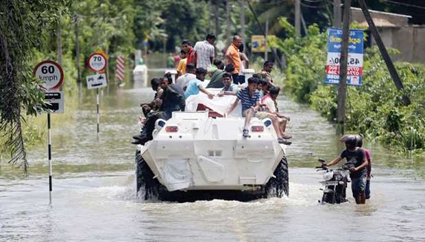 People being transported on top of an armoured personnel carrier on a flooded road as a man pushes his bike through the water in Kalutara yesterday.