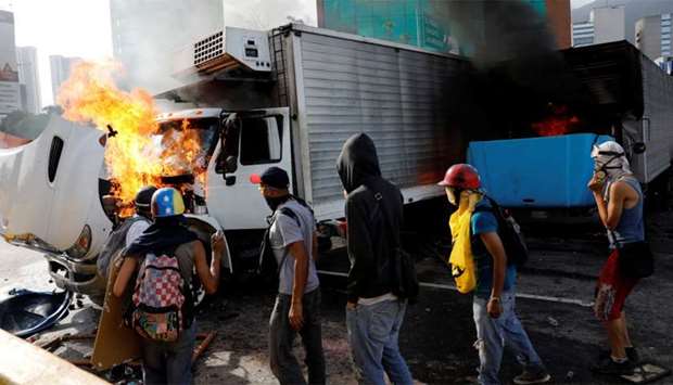 Demonstrators near trucks, which have been set on fire while clashing with riot security forces