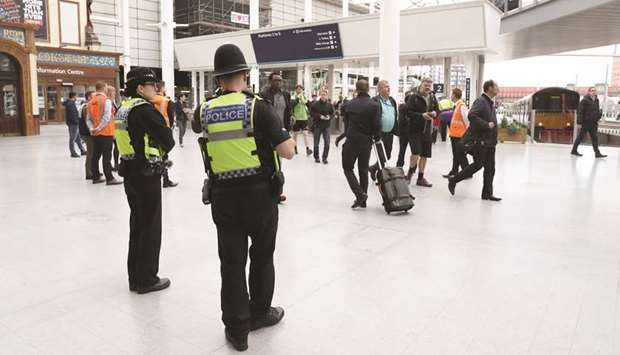 Police watch as commuters arrive at Manchester Victoria railway station yesterday. The station reopened yesterday for the first time since the carnage in which 22 people were killed.