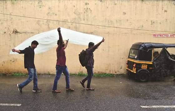 Men use a plastic sheet to cover from rain as they walk along a road in Kochi, Kerala yesterday.