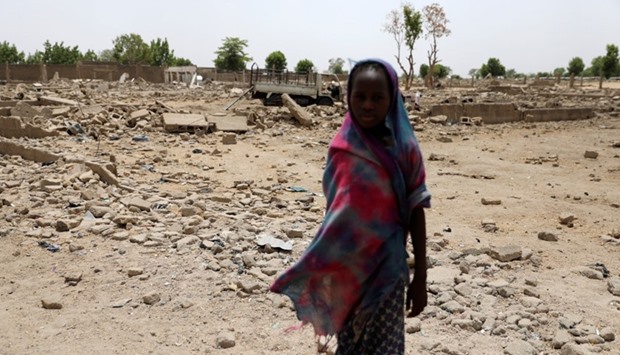 A girl stands before ruined homes in front of the IDP camp in Banki, Borno, Nigeria.