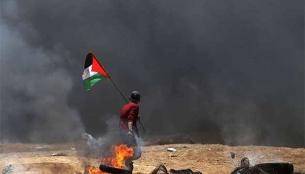 A Palestinian man drags burning tyres in the smoke during clashes with Israeli forces along the border with the Gaza Strip east of Khan Yunis on Monday.