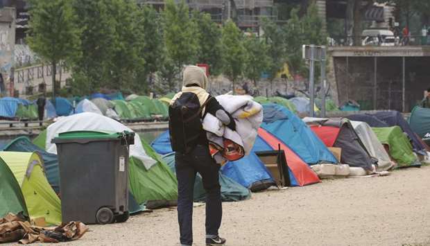 A migrant carries a blanket as he walks past tents where migrants live in a makeshift camp along the Quai de Valmy and Quai de Jemmapes of the canal Saint-Martin in Paris.