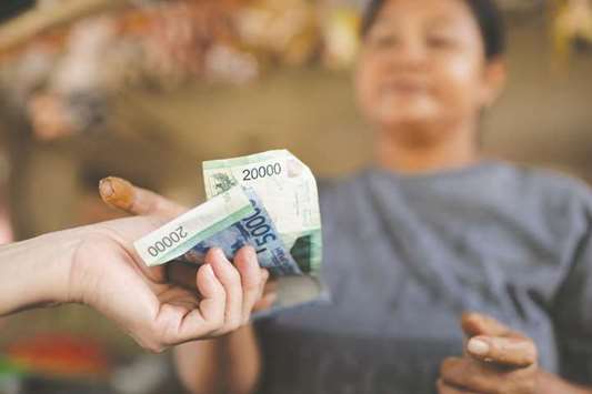 A customer hands Indonesian rupiah banknotes to a vendor at a stall at a market in Jakarta (file). In Indonesia, the central bank raised interest rates for the first time in three-and-a-half years after the rupiah fell to the weakest level since October 2015. Foreign investors are net sellers of about $2.9bn of Indonesian stocks this year, turning its equities into the worst performer in Asia.