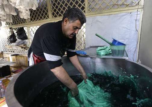 Mohamed al-Rihawi dips silk threads into green dye at his atelier in the Syrian capital Damascus.