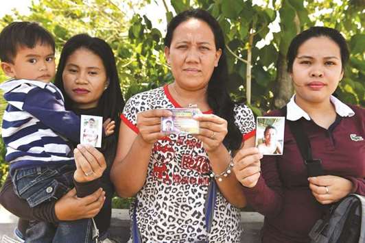 (From left) Alma Tome, Evelyn Powao, and Melgie Powao, whose husbands are still missing one year after the Marawi siege, show photos of their husbands during an interview in Iligan city on the southern island of Mindanao.