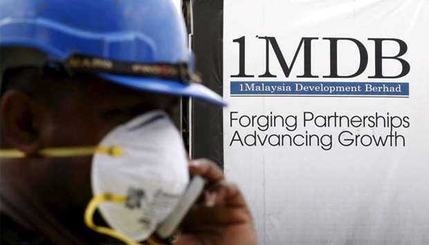 A construction worker talks on the phone in front of a 1Malaysia Development Berhad (1MDB) billboard
