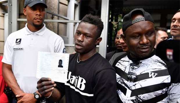 Malian migrant Mamoudou Gassama, flanked by his older brother (right), holds his temporary residence permit after he received it at the prefecture of Bobigny, northeast of Paris, on Tuesday.