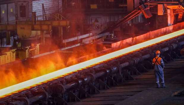 A red-hot steel plate passes through a press at a steel plant