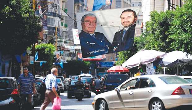 Cars and pedestrians pass a huge electoral campaign banner bearing portraits of Beirut district candidates, Nouhad Mashnuq (left) and Prime Minister Saad Hariri, yesterday.
