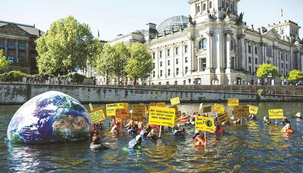 Greenpeace activists hold up posters as they swim with an inflatable globe through the river Spree past the Reichstag building housing the Bundestag (lower house of parliament) in Berlin.