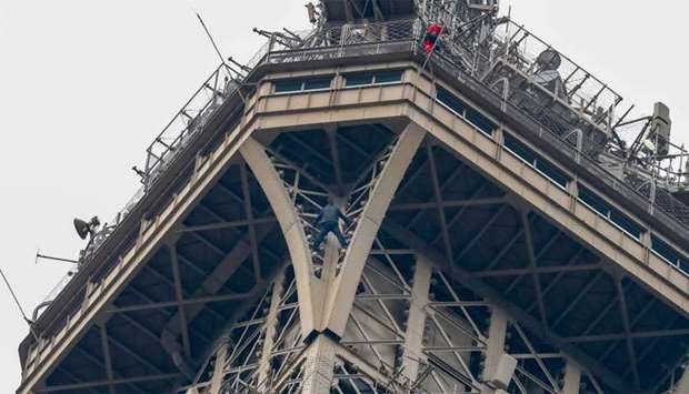 A man (C) climbs up the Eiffel Tower, in Paris, without any protection as a firefighter (R) looks down at him from the top
