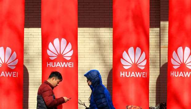 People walk past logos of Huawei