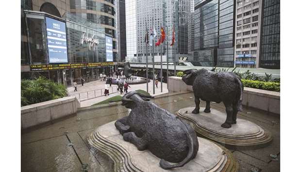 Sculptures of water buffaloes stand as pedestrians walk past an electronic ticker board and screens displaying stock figures outside the Exchange Square complex, which houses the Hong Kong Stock Exchange. Hong Kong was among the worst performers in Asia with the Hang Seng Index diving 1.6% to 27,267.13 points yesterday.