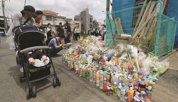 People pay their respects next to flower tributes at the crime scene where a man stabbed 19 people, including children, in Kawasaki, yesterday.