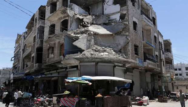 People walk past a damaged building in the city of Idlib