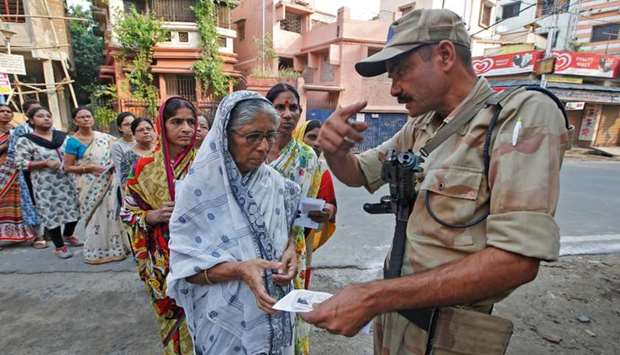 A security personnel checks the identity card of a woman as she stands in a queue with others to cast their vote at a polling station during the fifth phase of general election in Howrah, on the outskirts of Kolkata