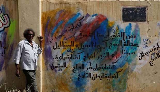 Rashid Drar poses next to a graffiti of him near the defence ministry compound in Khartoum